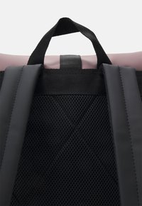 Bretelles de sac à dos rembourrées noires et panneau arrière en mesh avec une boucle de poignée cousue sur un fond clair.