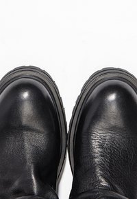 Paire de bottes en cuir noir avec des bouts arrondis et des semelles épaisses en caoutchouc sur fond blanc.
