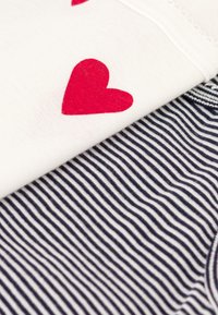 Witte stof met rode hartmotieven bovenop navy- en witte gestreepte stof creëren een gelaagd textielontwerp. Beide zijn van katoen.