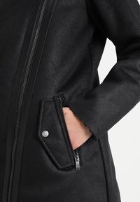 Černá umělá kožená bunda s hladkým povrchem, boční zipovou kapsou a centrálním zipem. Design zahrnuje minimalistickou siluetu.