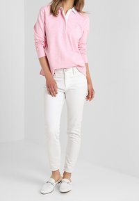 Helles rosa Langarmpolo mit weißem Kragen, kombiniert mit engen weißen Jeans und weißen Slippern, zeigt ein lässiges Outfit.