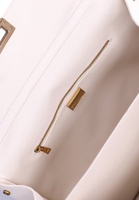 Interno di una borsa in pelle rosa chiaro con una tasca con zip dorata e una placca metallica con il marchio. Texture liscia; design minimalista senza motivi.