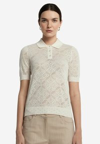 Stickad polo i krämfärgad med diamantmönster, korta ärmar och krage med knapppdetaljer framtill.