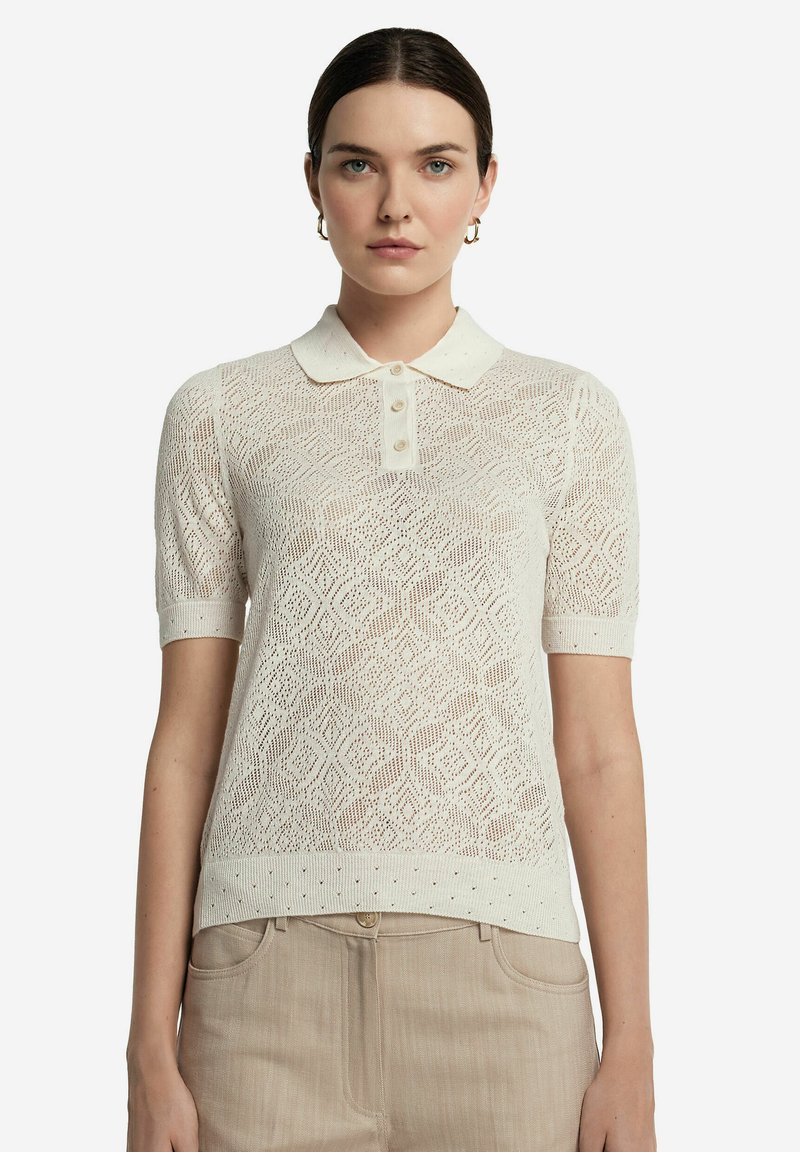 Stickad polo i krämfärgad med diamantmönster, korta ärmar och krage med knapppdetaljer framtill.