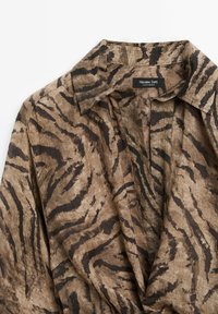 Lettet skjorte i beige med brun tigerstribemønster. Har en spidse krave og knaplukning foran, lavet af linned.