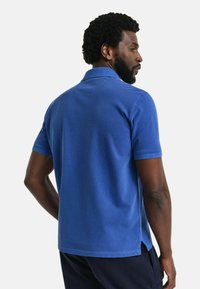 Sininen puuvillapaita, jossa on lyhyet hihat, klassinen kaulus ja sivuhalkiot helman kohdalla lisäämään liikkuvuutta ja mukavuutta.