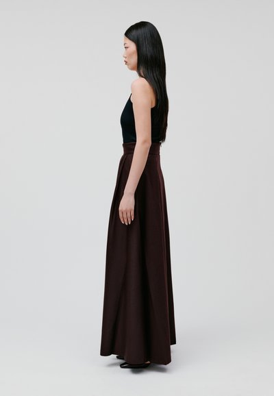 Black sleeveless top paired with a long, burgundy skirt featuring a high waist and pleats, worn with black pointed-toe heels.