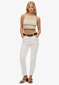 Gehaakte haltertop met meerkleurige strepen, gecombineerd met witte high-waisted broek en eenbruine riem. Sandalen met blokhak en open tenen.