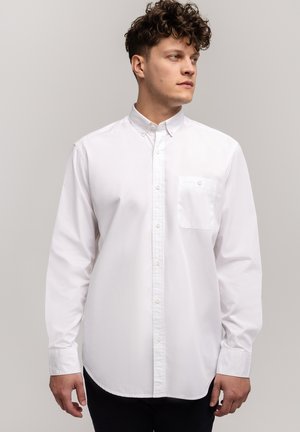 Biała koszula typu button-down wykonana z bawełny, z klasycznym kołnierzykiem, kieszonką na lewej piersi i długimi rękawami. Gładka faktura, dopasowany krój.