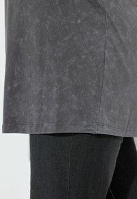 Šedá, texturovaná tunika s volným střihem, sahající do poloviny boků, v kombinaci s černými, přiléhavými džíny. Minimalistický design, bez viditelných vzorů.
