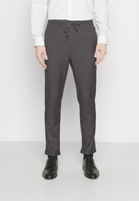 Pantaloni grigi con cintura con cordoncino, gambe a sigaretta e risvolti, realizzati in un tessuto testurizzato. Abbinati a scarpe eleganti nere.