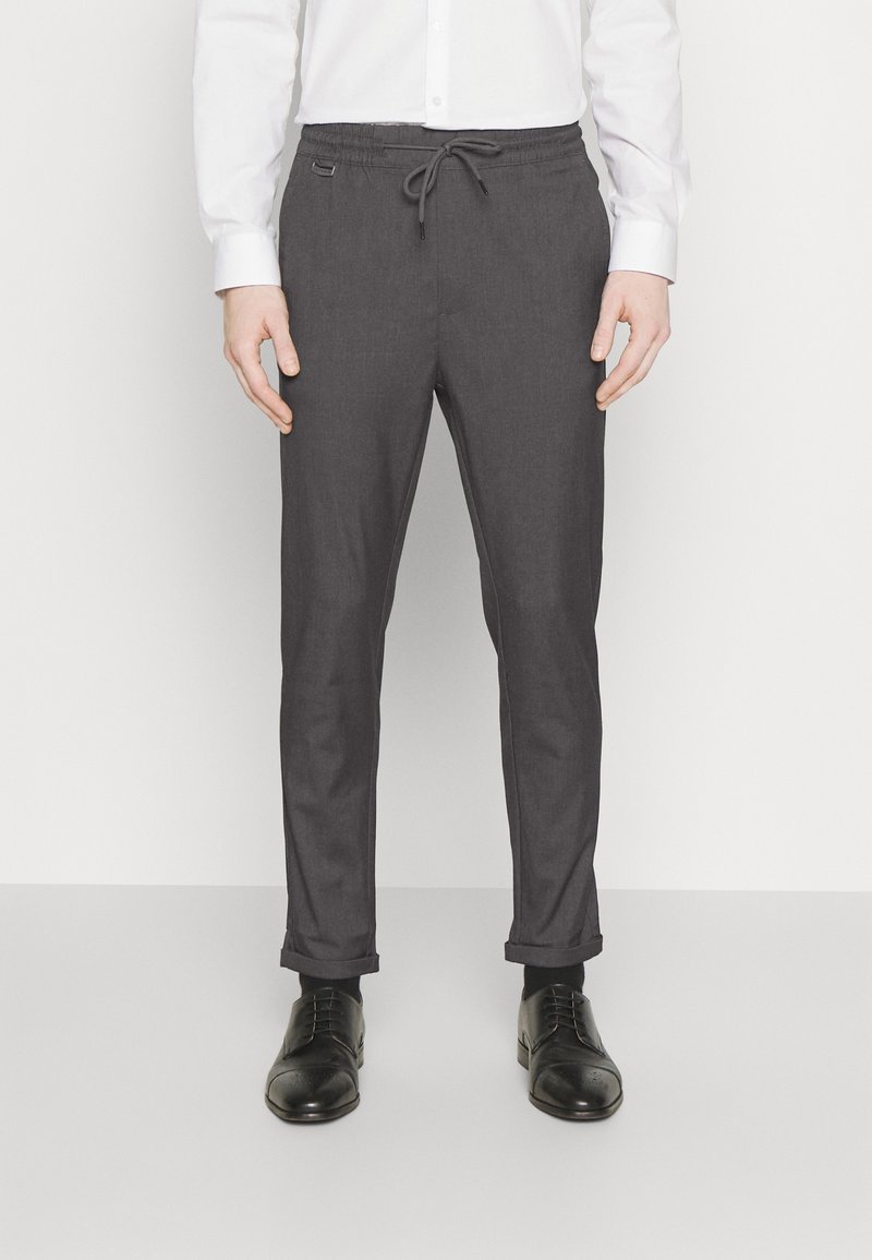 Pantaloni grigi con cintura con cordoncino, gambe a sigaretta e risvolti, realizzati in un tessuto testurizzato. Abbinati a scarpe eleganti nere.