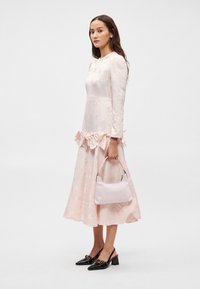 Μακρύ ροζ φόρεμα με λουλουδάτο κέντημα, ριχτή μέση, συνδυασμένο με μια ανοιχτό ροζ τσάντα και μαύρες ψηλοτάκουνες γόβες. Λείος υφασμάτινος τύπος.