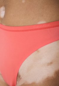Koraal kleurige Calvin Klein bikini bottom met een gladde textuur, elastische tailleband en een minimalistisch ontwerp. Zichtbaar logo detail nabij de taille.
