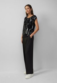 Schwarzes kurzärmliges Oberteil mit metallicfarbigem Textdesign, kombiniert mit schwarzen weit geschnittenen Hosen und weißen Sneakern. Minimalistischer, glatter Stofftextur.