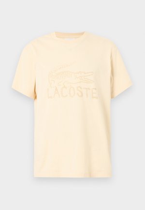 Camiseta con logo de Lacoste en amarillo pastel claro. Hecha de algodón, cuenta con cuello redondo y mangas cortas con diseño bordado de cocodrilo y nombre de la marca.