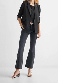 Black tailored blazer, cropped black top, dark denim flared jeans, and silver strappy heels. Smooth fabric with structured design details.
