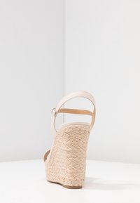 Sandalo con zeppa beige con tacco in juta intrecciata, cinturino alla caviglia e tomaia in pelle liscia. Presenta una punta arrotondata e una suola texturizzata.