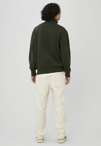 Pull vert foncé en maille avec un col montant, associé à un pantalon en velours côtelé beige clair avec un motif subtil.