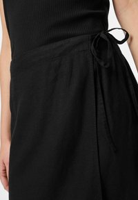 Černá lněná sukně s uchem v pase, s čistým, skládáním designem a mírně texturovaným povrchem.