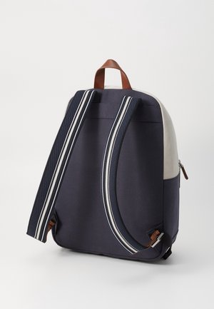 Navy and white backpack with padded striped shoulder straps and brown leather handle, shown from the back on a white background.