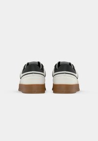 White and black sneakers with a gum sole, featuring a smooth upper, textured accents, and a logo at the heel.