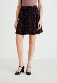 Saias pretas com evasê e pequeno padrão floral vermelho. Tecido suave e leve com cintura elástica. Combinada com sapatos Mary Jane pretos em verniz.