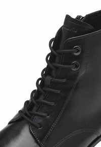 Bottines en cuir noir avec lacets ronds, un col haut et une finition lisse avec de légers détails de couture et des œillets en métal.