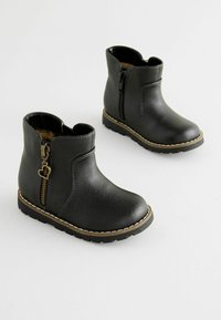Schwarze Stiefeletten aus Kunstleder mit einem seitlichen Reißverschluss und einem herzförmigen Ziehen, die eine strukturierte Oberfläche und kontrastierende helle Nähte aufweisen.