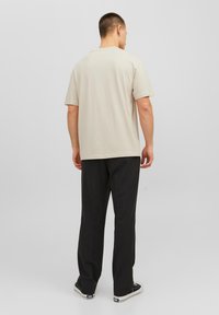Beige short-sleeve t-shirt with a relaxed fit, crew neck, and soft texture, paired with black loose-fitting trousers and black sneakers.