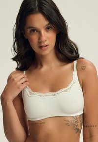 Biały biustonosz braletka z delikatnym koronkowym wykończeniem przy dekolcie, wykonany z miękkiego materiału, z regulowanymi ramiączkami. Posiada bezszwowy krój dla większego komfortu.
