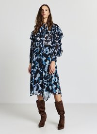 Abito in chiffon fluido con una stampa astratta blu e nera; maniche lunghe a volant e dettaglio al collo con fiocco; abbinato a stivali alti fino al ginocchio in suede marrone.