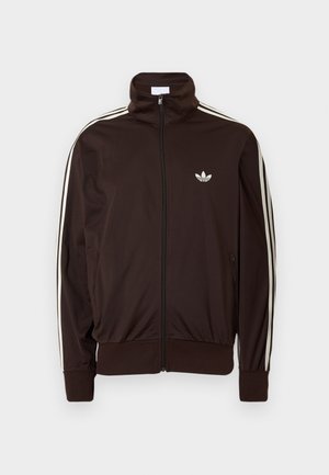 Tmavě hnědá sportovní bunda na zip se třemi bílými pruhy podél rukávů a malým bílým logem Adidas trefoil na hrudi.