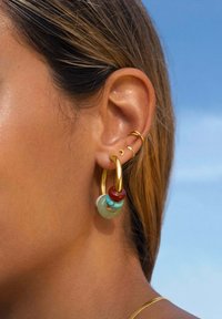 Boucle d'oreille en or avec des perles colorées (rouges, turquoise et vertes). Surface métallique lisse avec des formes et des couleurs de perles variées.
