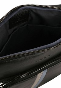 Bolso de cuero negro con cierre de cremallera, que presenta un interior azul marino y una etiqueta. Adornado con rayas grises y azul claro en un lado.