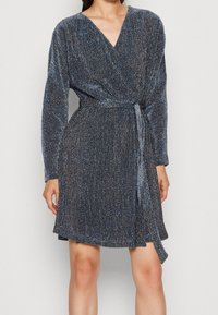 Robe portefeuille bleu métallique à manches longues, tissu texturé, encolure en V, taille cintrée et ceinture nouée. Caractérisée par une jupe fluide.