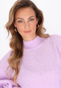 Pull en maille violet clair avec un col montant, présentant des accents de fil argenté et des manches amples. Texture douce et détails de design côtelés.
