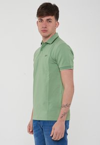 Polo verde con colletto, chiusura a bottoni e maniche corte. Presenta un orlo a contrasto e un piccolo logo sul lato sinistro del petto.