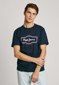 Navy plava pamučna majica s bijelim i crvenim logotipom koji glasi "Pepe Jeans London", okrugli izrez, kratki rukavi i ležeran kroj.