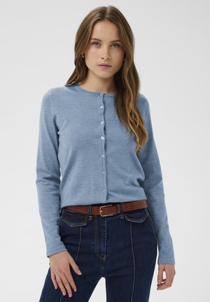 Lyseblå cardigan med rund halsudskæring, knaplukning foran og lange ærmer. Kombineret med mørkeblå jeans og et brunt bælte.