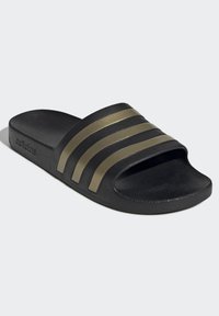 Black slide sandal with three gold stripes on the upper strap. Textured material with a flat sole and subtle logo on the side.