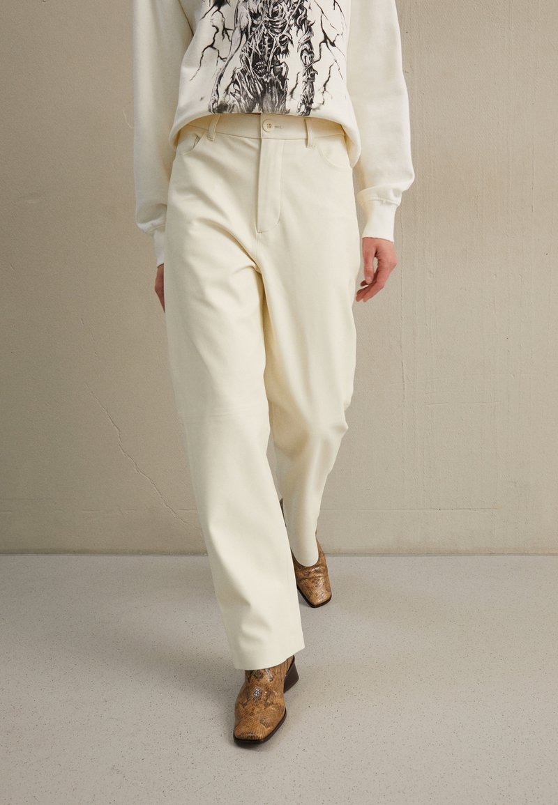 Krämfärgade vida byxor i kombination med en grafisk sweatshirt och bruna ormskinnsankelboots. Slätt tyg med en subtil lyster.