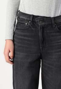 Black denim jeans with a straight fit, featuring five-pocket design, metal hardware, and a subtle texture. Paired with a light gray ribbed top.