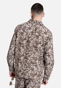 Υφασμάτινο μπέζ πουκάμισο με σκούρο καφέ λουλουδάτο μοτίβο, μακριά μανίκια, κουμπωτό μπροστινό μέρος και λεπτομέρειες στον ώμο στην πλάτη, συνδυασμένο με παντελόνι που ταιριάζει.