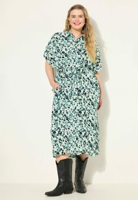 Kukkaistapettia oleva mintunvihreä mekko, jossa on lyhyet, leveät hihat, kireä vyötärö ja sivutaskut, yhdistettynä polven korkeisiin mustiin cowboy-kengiin.