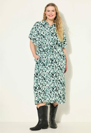 Robe mint à motifs floraux avec des manches courtes et larges, taille cintrée et poches latérales, associée à des bottes de cow-boy noires jusqu'aux genoux.