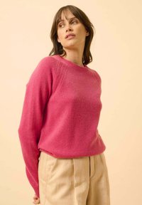 Maglione rosa a maglia con scollatura rotonda e maniche raglan, caratterizzato da una texture morbida e una vestibilità casual, abbinato a pantaloni beige.