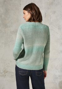 Mintgrön stickad tr�öja med ribbad textur, rundad halsringning och långa ärmar, kombinerad med mörka jeans.