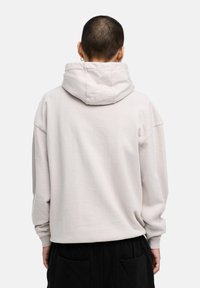Light gray hooded sweatshirt made of soft cotton. Features a relaxed fit, dropped shoulders, and ribbed cuffs. Background is plain.