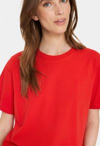 Tricou roșu din bumbac, cu mâneci scurte și decolteu rotund, având o textură netedă și o croială lejeră.